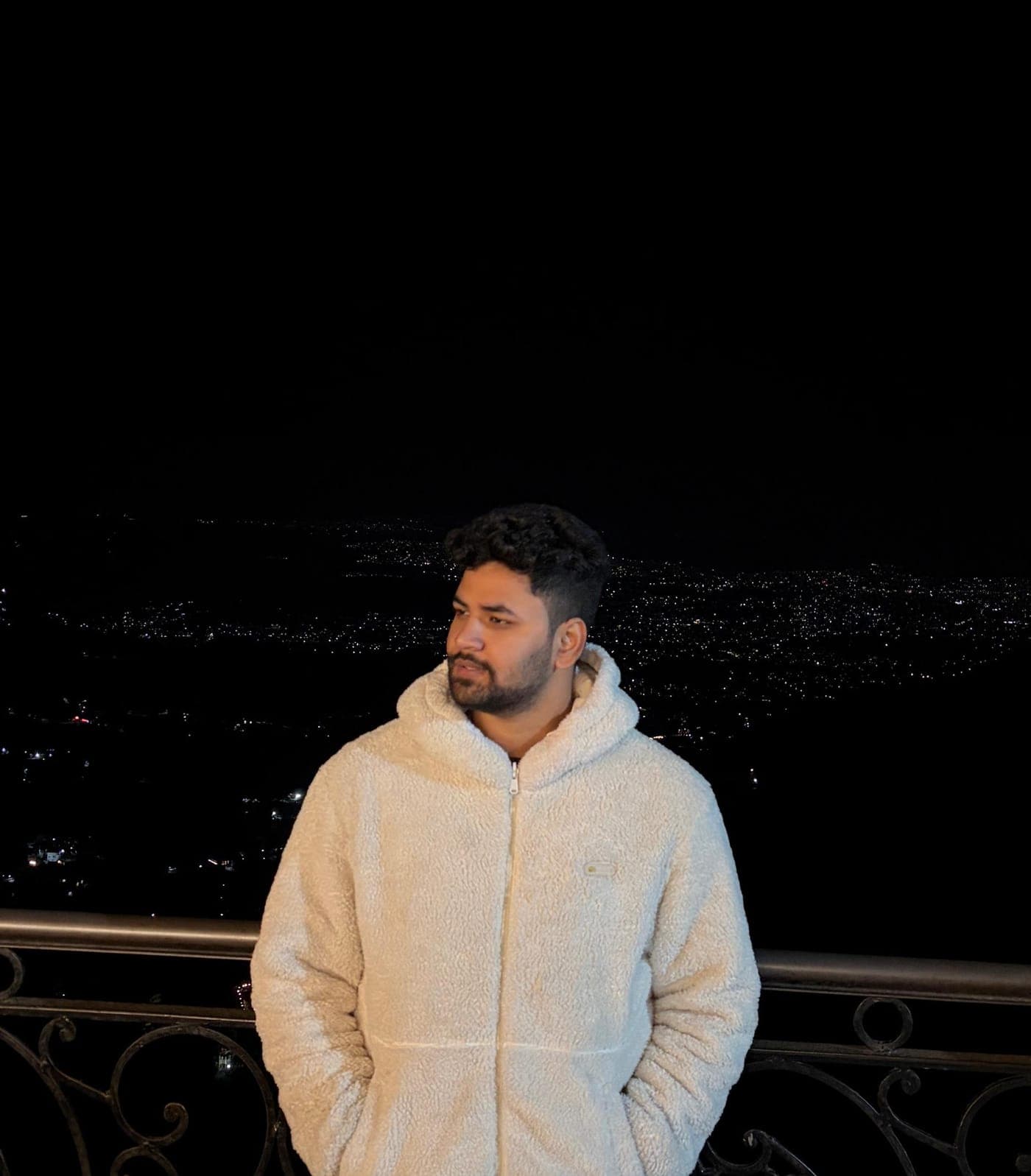 Tarush at a railing at night, city lights spread across the valley below