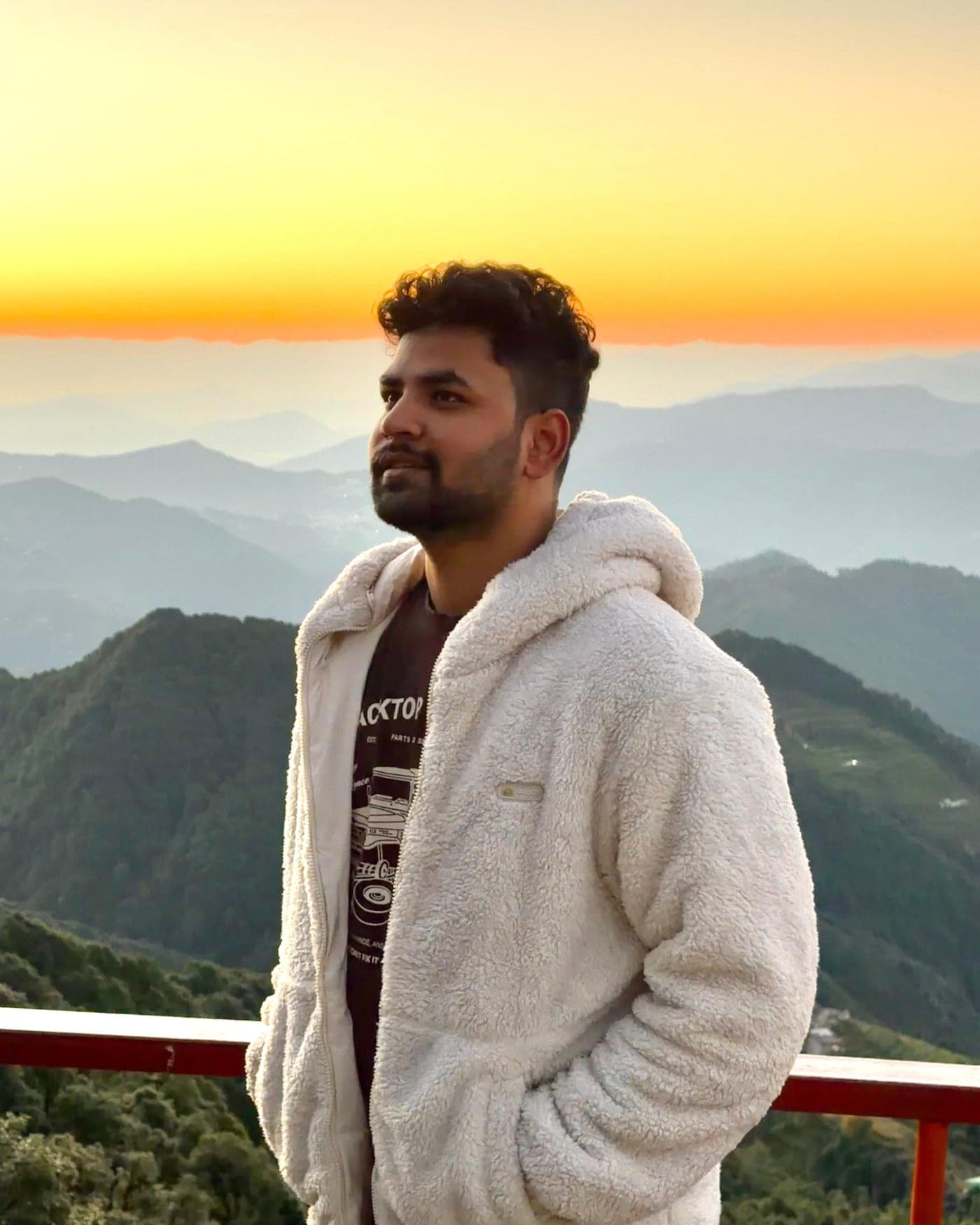Tarush Kumar in a white jacket, mountains and a sunset horizon behind him